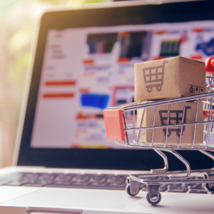 A laptop computer with a small shopping cart placed on it, symbolizing e-commerce in 2024."